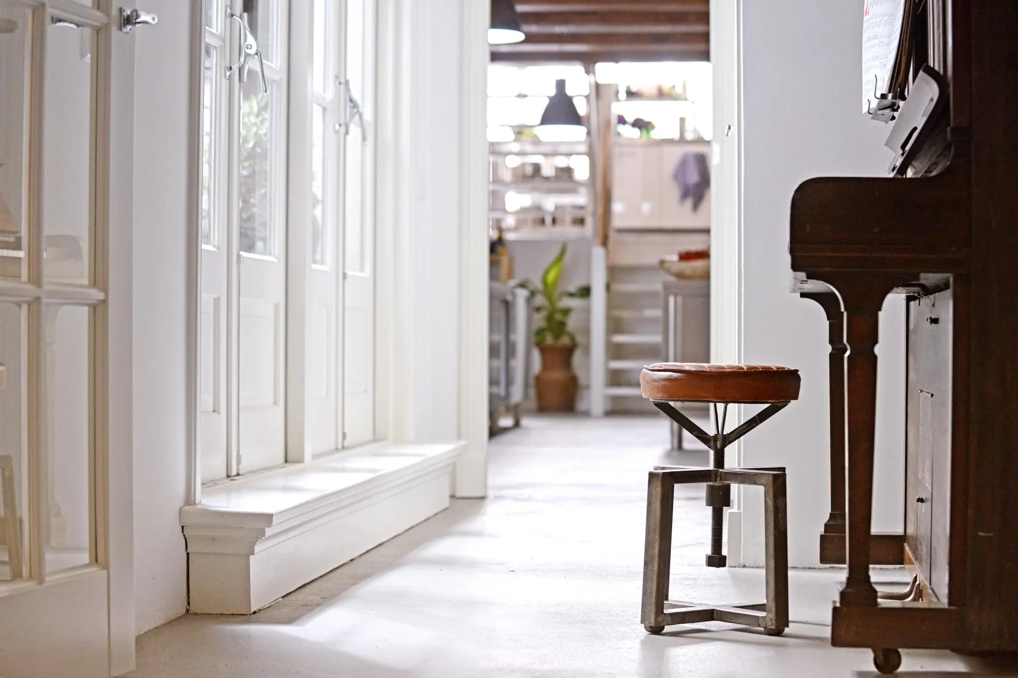 Licht en sfeervol interieur met een pianokruk naast een piano in een gang aan de Nieuwe Kerkstraat.